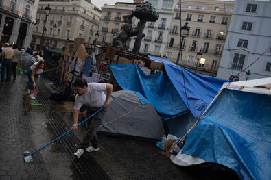 Varias personas desaguando sus tiendas de campaña en la Puerta del Sol, tras las lluvias de este sábado sobre el centro de la capital.
